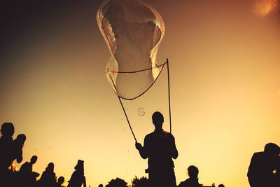 Low angle view of silhouette man blowing giant bubble from wand during sunset
