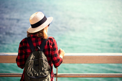 Rear view of woman standing by railing against sea