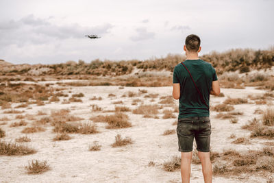 Rear view of young man flying drone standing on field