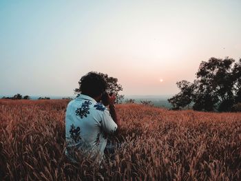 Rear view of person standing on field against sky during sunset