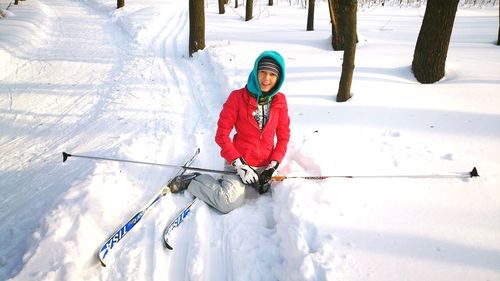 Woman with skis sitting on snow covered field