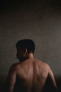 Rear view of shirtless man looking away against wall