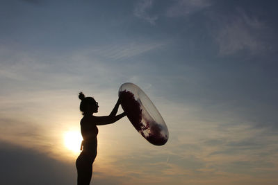 Side view of silhouette woman holding inflatable raft while standing against sky during sunset