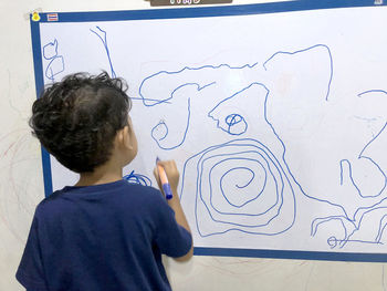 Rear view of boy drawing on paper stuck at wall