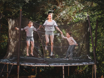 Three beautiful caucasian sister girls in jeans, shorts and a sleeved t-shirt jump on a trampoline