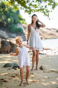 Full length of mother and daughter standing at beach