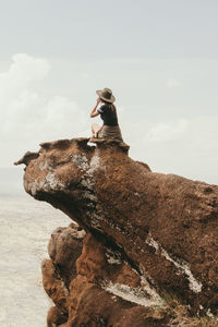 Woman sitting on rock formation by sea against sky