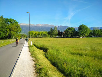 People walking on field by road against sky