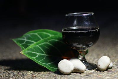 Close-up of wineglass with pebbles and leaves at night