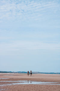 People horseback riding on land against sky