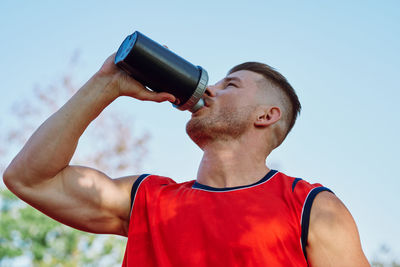 Low angle view of man drinking water against sky