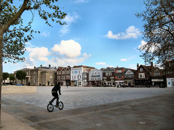 Woman walking on sidewalk against cloudy sky