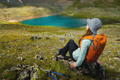 Nice woman in a panama with a backpack sits on a stone, having a rest after trekking in the