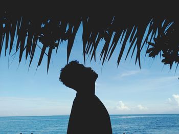 Side view of silhouette young man standing by sea against sky