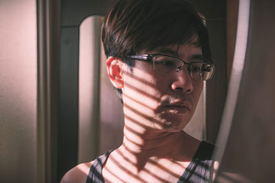 Close-up portrait of young man looking through window at home