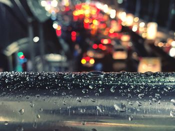 Close-up of wet steel against illuminated city during rainy season