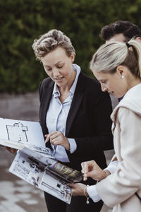 Confident agent showing magazine of new property to couple outdoors