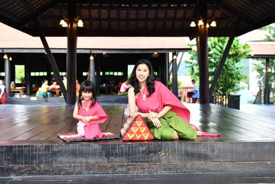 Portrait of mother and daughter in traditional clothing sitting on wooden floor