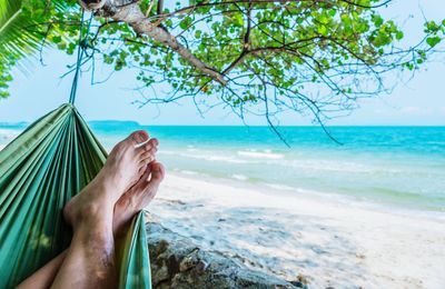 Low section of man relaxing on hammock at beach