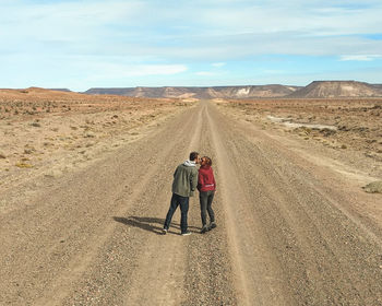 Rear view of man walking on dirt road against sky