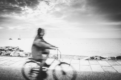Man riding bicycle by sea against sky