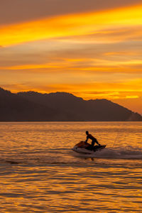 Silhouette man surfing in sea against sky during sunset