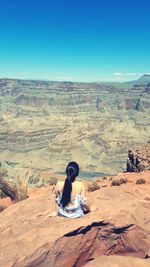 Woman sitting on desert against clear sky