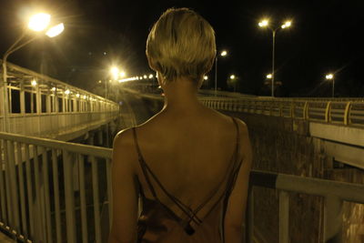 Rear view of woman standing by railing against sky at night