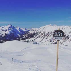 Road sign on snow covered mountain against blue sky