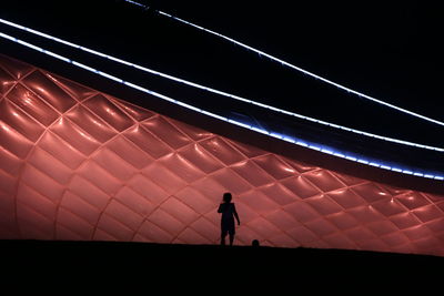 Silhouette man standing on illuminated road at night