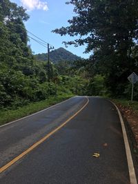 Empty road by trees against sky
