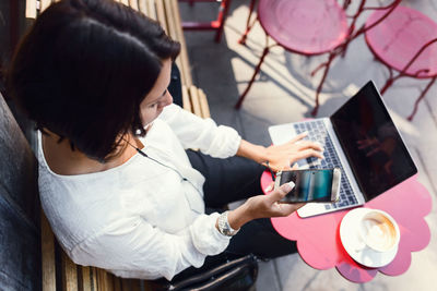 High angle view of businesswoman using smart phone and laptop at sidewalk cafe