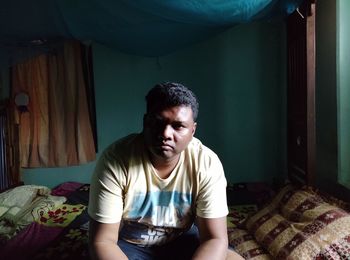 Portrait of young man sitting on bed at home