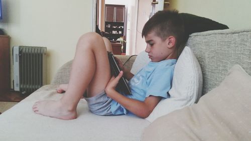 Side view of boy using digital tablet on sofa at home