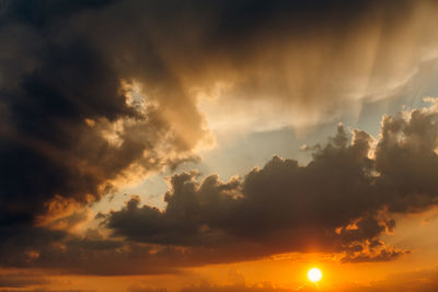 Low angle view of sunlight streaming through clouds during sunset