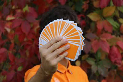 Close-up of hand holding cards against autumn tree