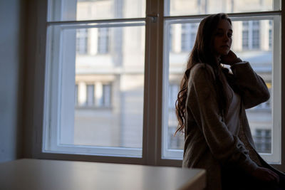 Portrait of woman sitting against window at home