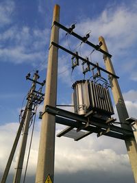 Low angle view of electricity poles against the sky