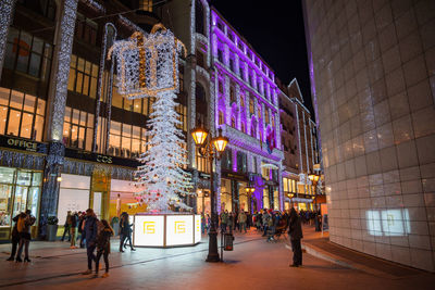 People walking on illuminated street amidst buildings at night