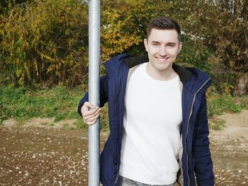 Portrait of smiling young man standing by pole against plants