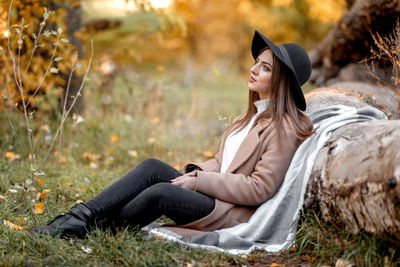 Thoughtful woman leaning wooden log at park