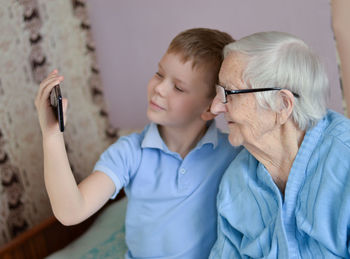 Happy elderly 90-year-old woman with glasses  and her grandsone smiles using a smartphone.