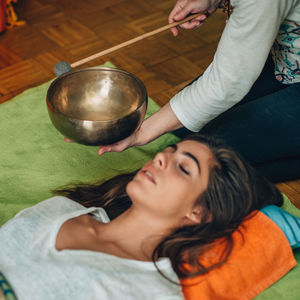 Midsection of therapist playing rin gong by young woman at spa