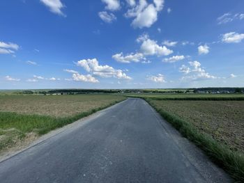 Empty road amidst field against sky