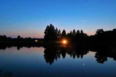 Reflection of silhouette trees in lake against sky during sunset