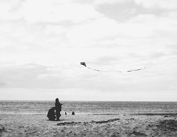 People flying kite at beach against cloudy sky