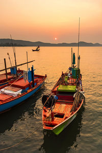 Fishing boat moored in sea against sky during sunset