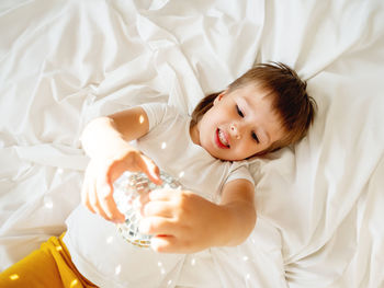 Little boy plays with sparkling mirror disco ball in bed and laughing happily. joyful toddler. 