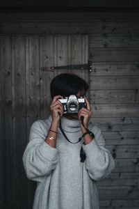 Portrait of woman photographing against wooden wall