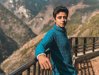 Portrait of young man standing against railing